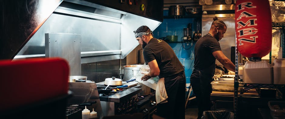 Two chefs preparing meals in a bustling restaurant kitchen, focused on culinary tasks.
