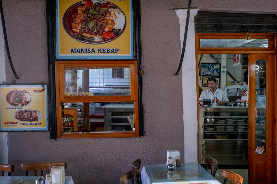 Cozy indoor view of a Turkish restaurant with Manisa kebab posters and a waiter at the counter.