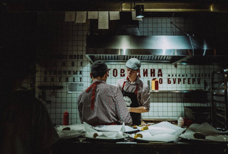 Chefs working in dimly lit kitchen, preparing food. Atmosphere is rustic and industrial.
